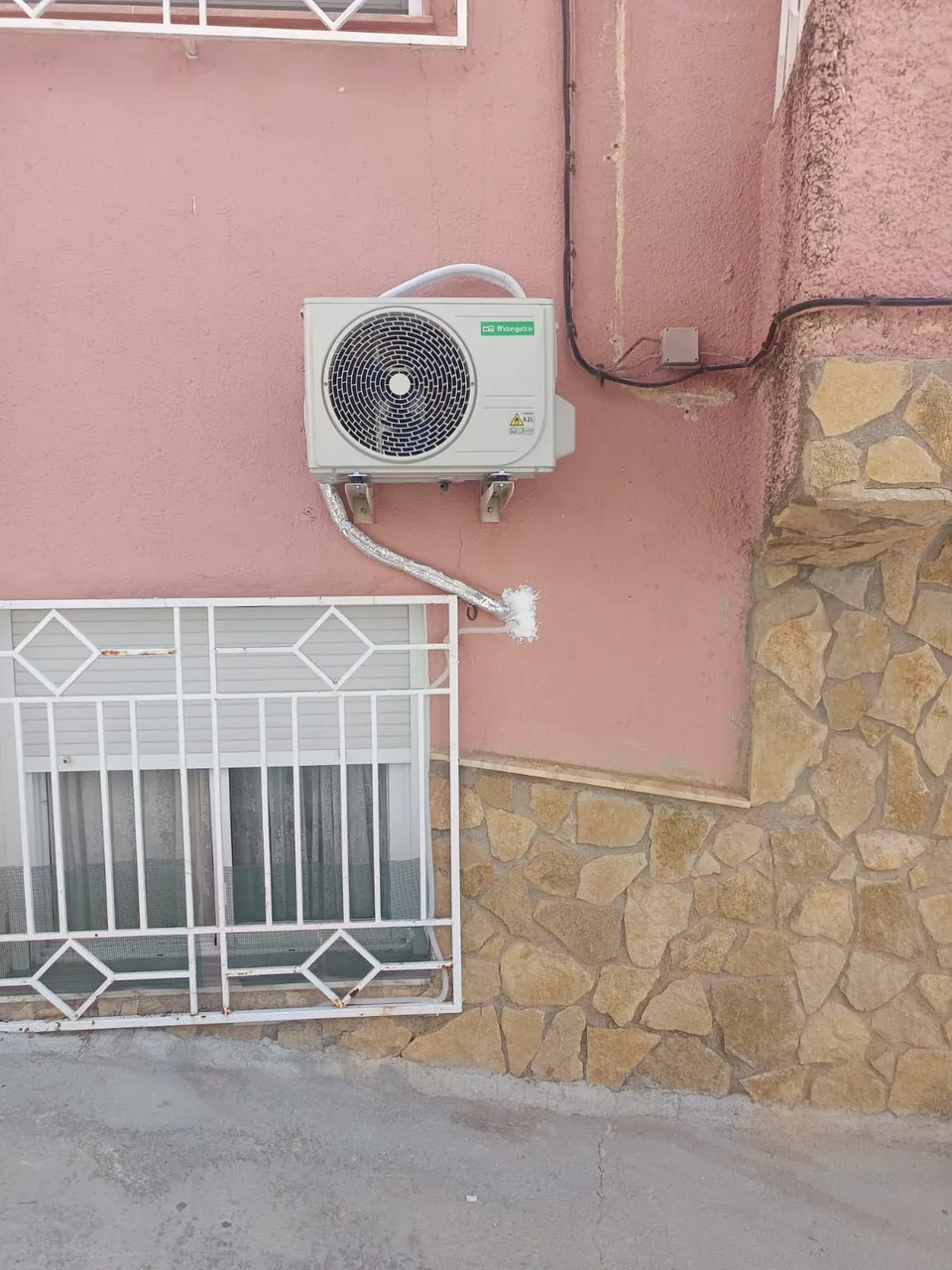Unidad exterior de aire acondicionado instalada en la fachada de una vivienda.