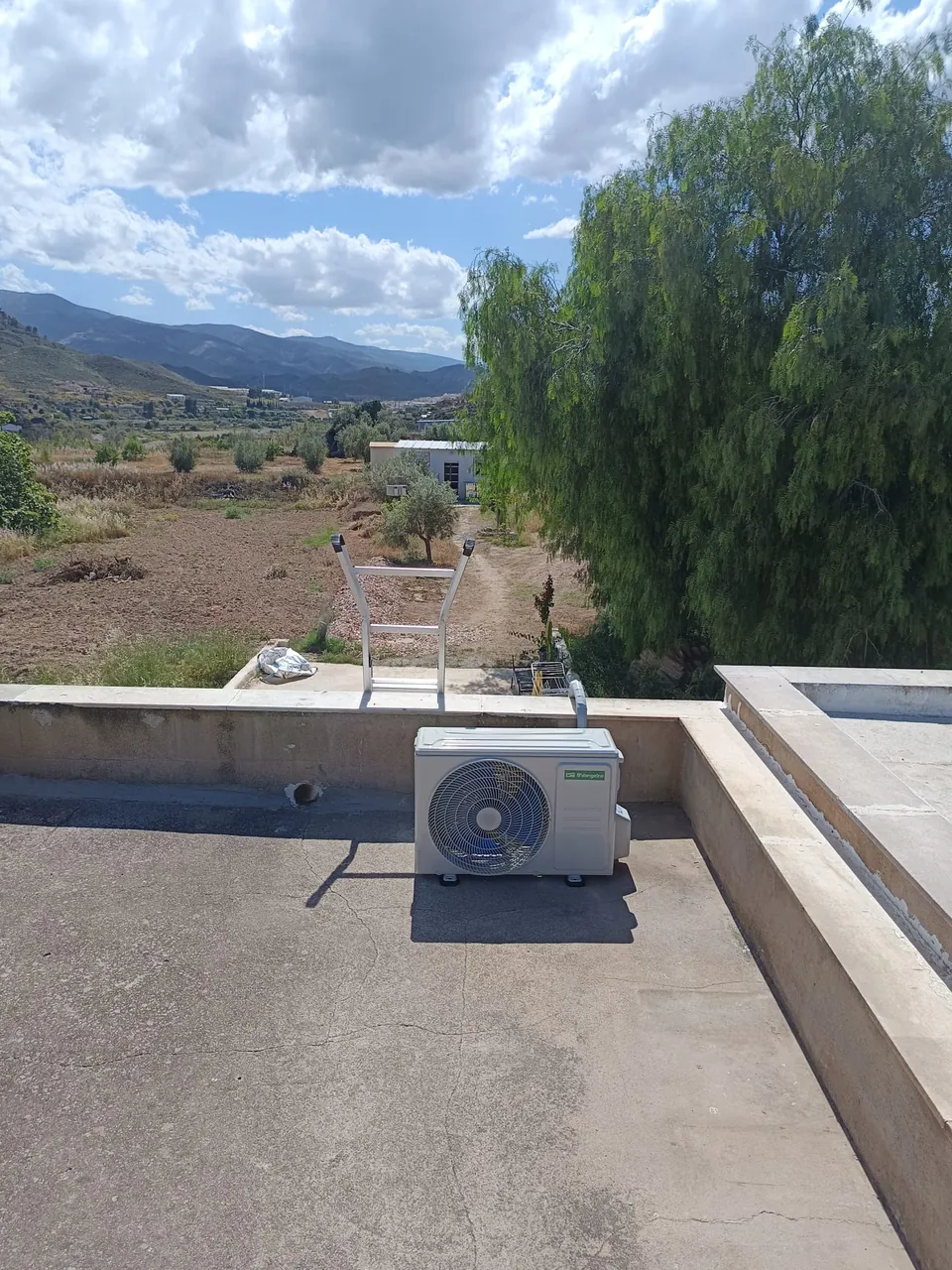 Unidad exterior de aire acondicionado instalada en una azotea con vistas al campo.