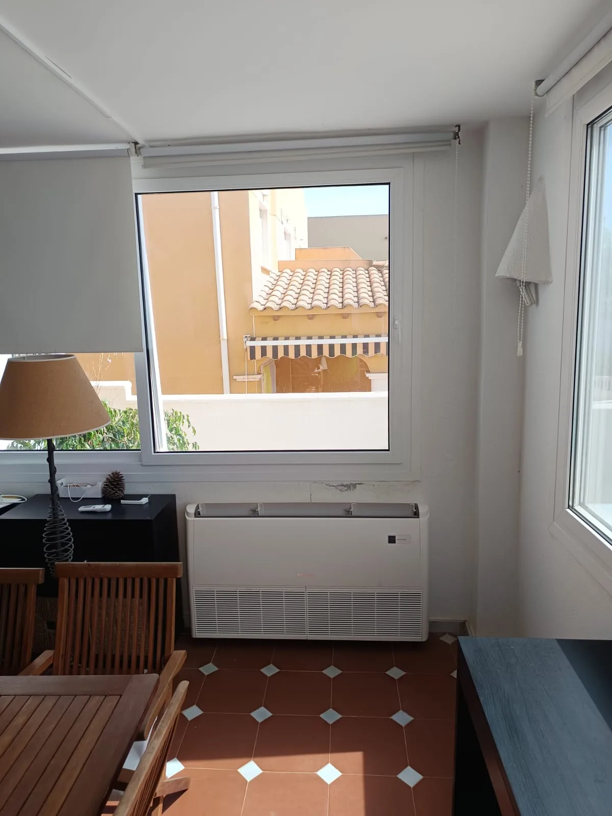 Unidad de aire acondicionado de consola suelo-techo instalada bajo la ventana de un salón.