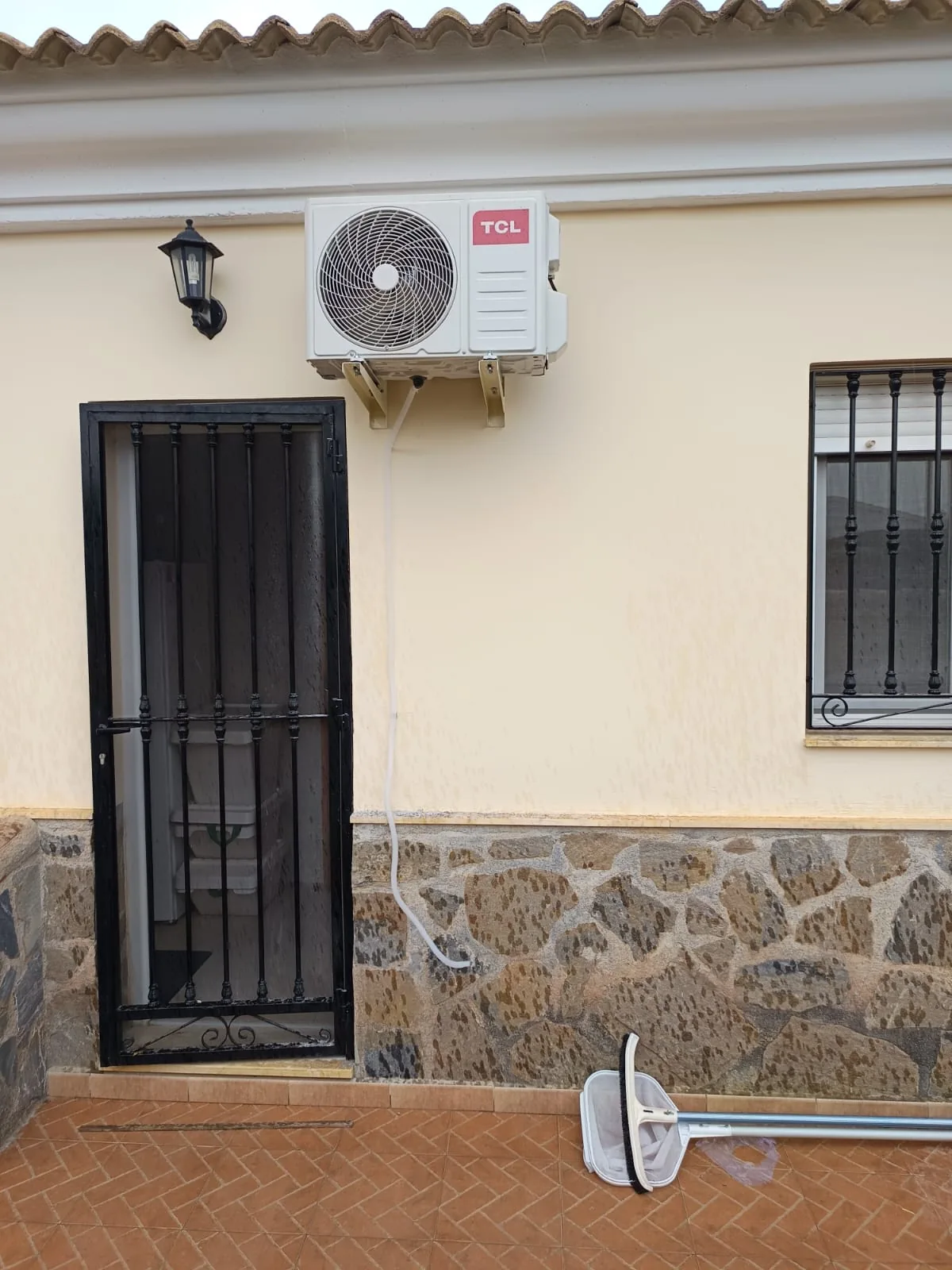 Unidad exterior de aire acondicionado instalada en la fachada de una casa de pueblo.