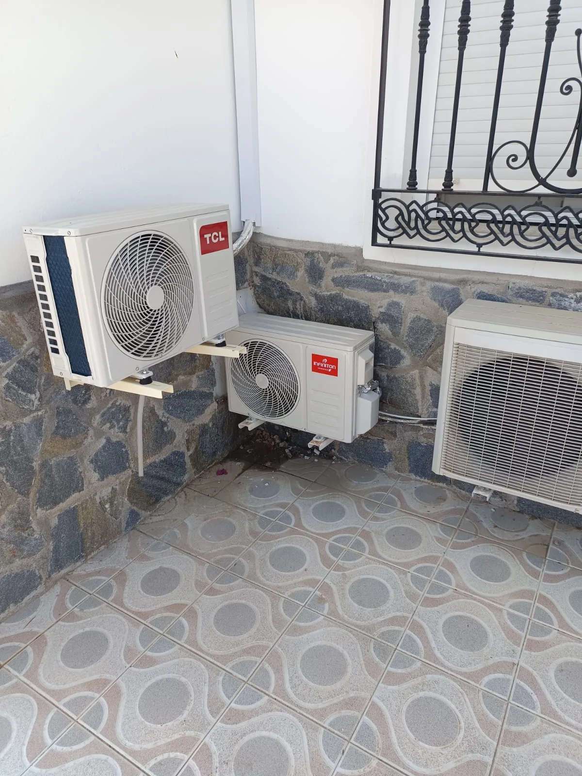 Tres unidades exteriores de aire acondicionado instaladas en un patio con zócalo de piedra.