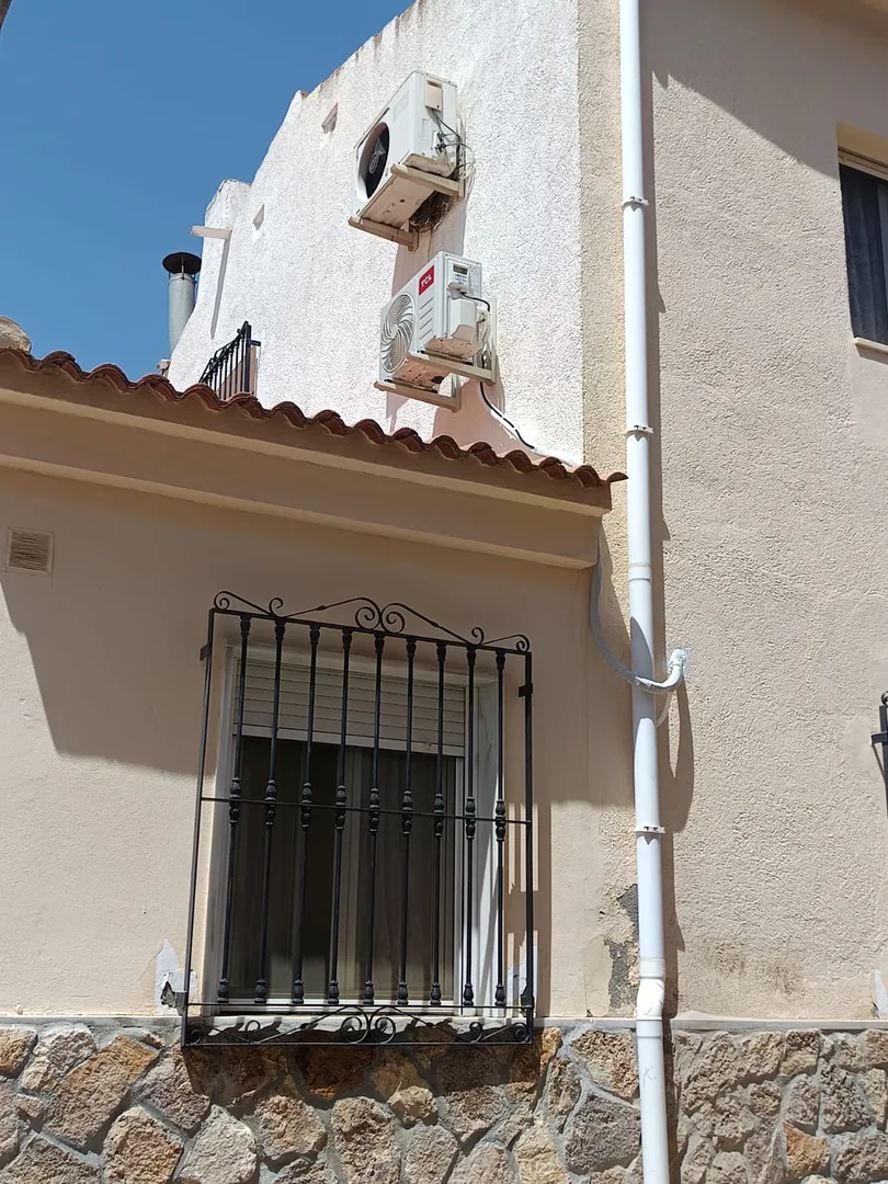 Unidad exterior de aire acondicionado instalada bajo el alero de una vivienda.