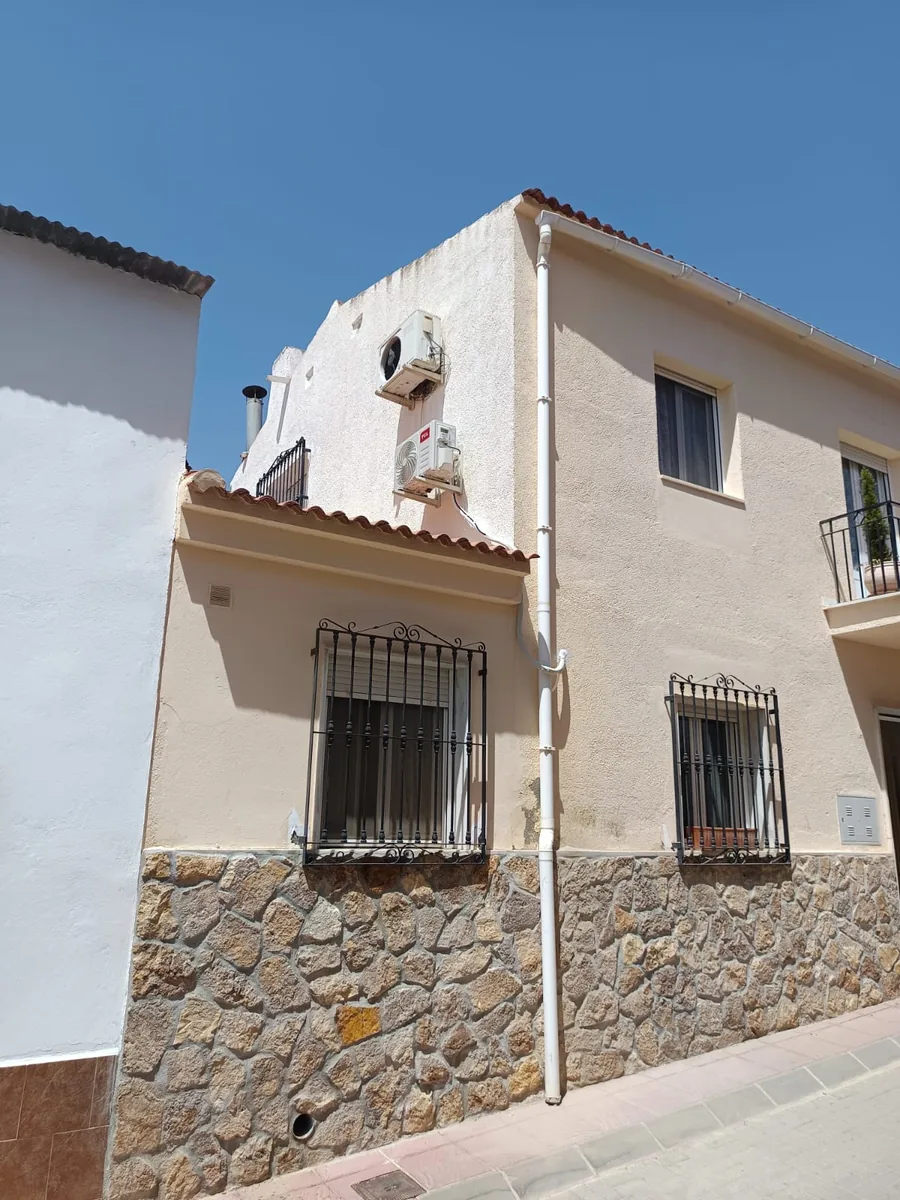 Unidad exterior de aire acondicionado en la fachada de una casa de dos plantas.