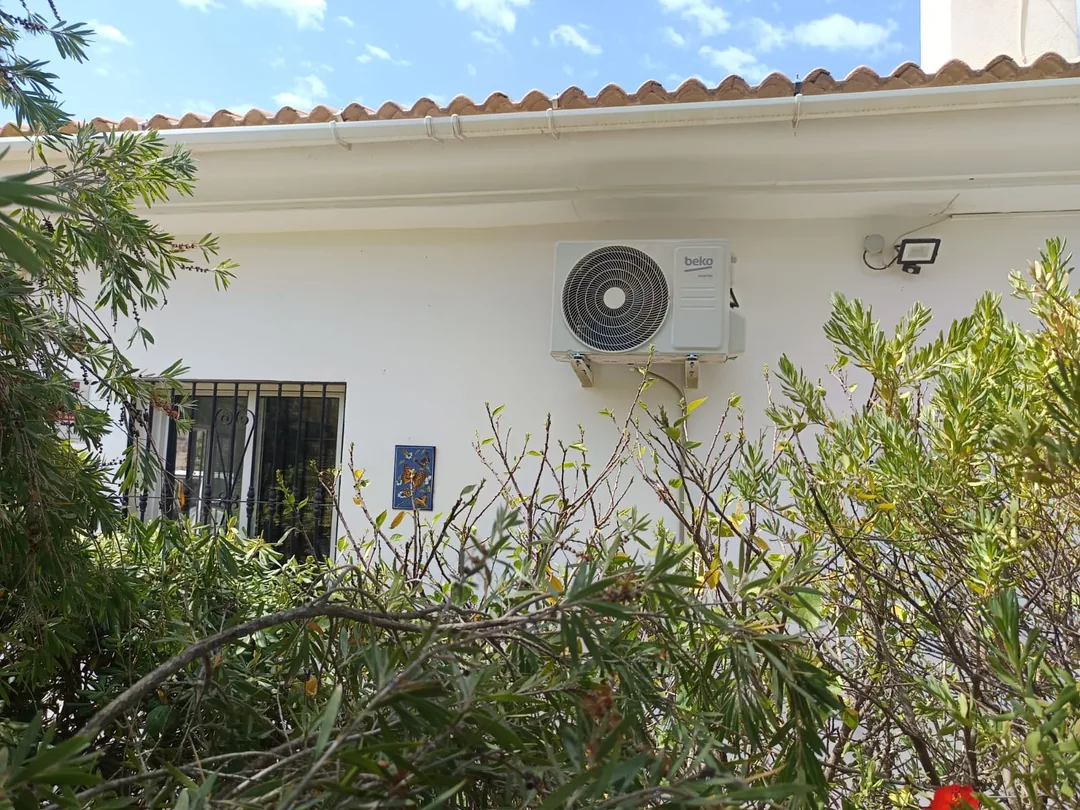 Unidad exterior de aire acondicionado en la fachada de una vivienda con jardín.