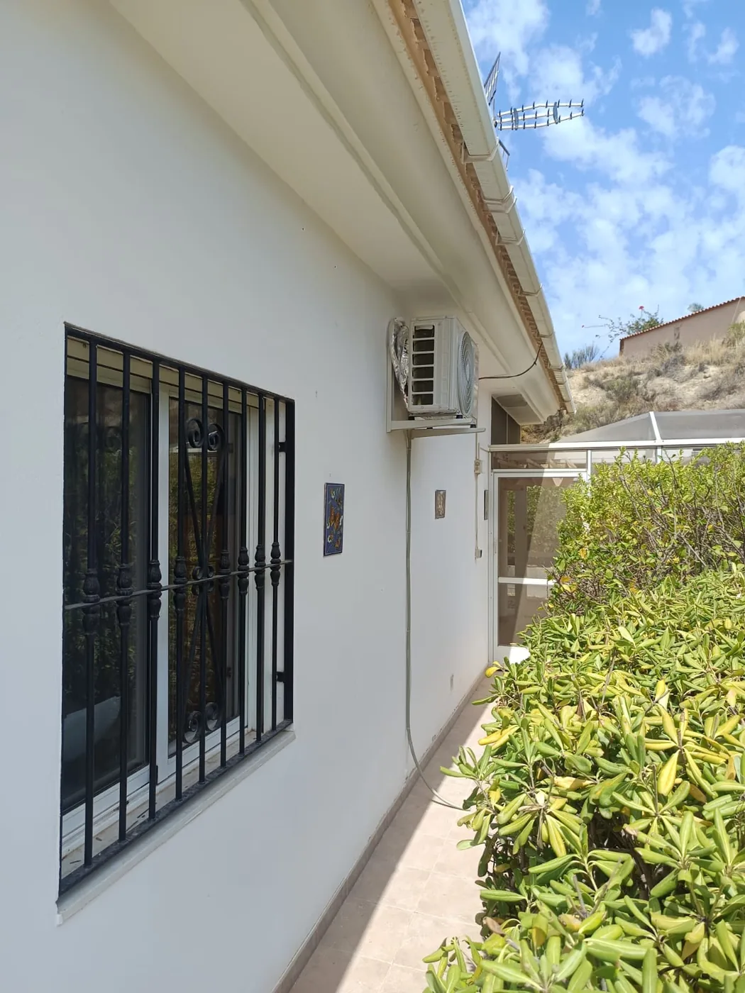 Unidad exterior de aire acondicionado y antena de televisión en el lateral de una vivienda.