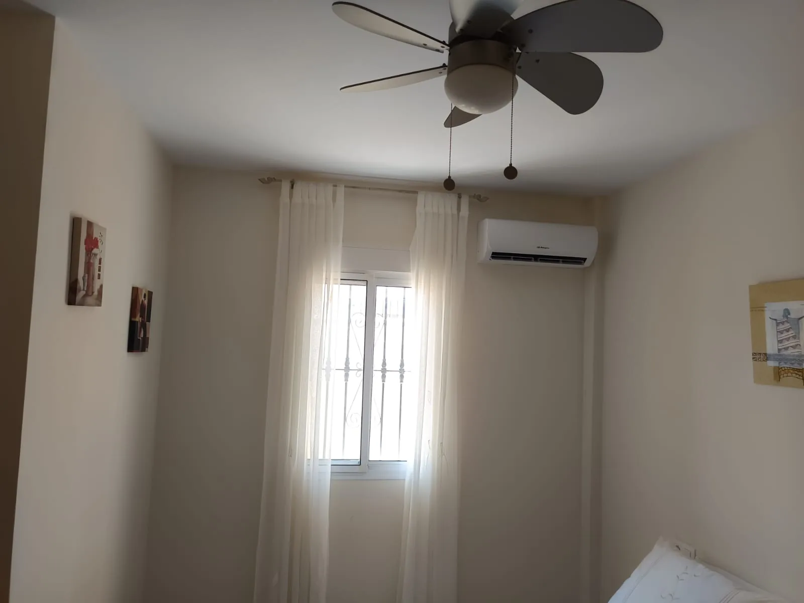 Split de aire acondicionado instalado en un dormitorio con ventilador de techo.